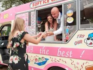A bride and groom serving one of their wedding guests from the window of the pink Fat Sam's ice cream van, which they hired for their wedding