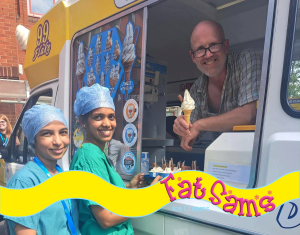 Two smiling NHS healthcare workers in green scrubs and blue hairnets stand outside Fat Sam’s yellow and white ice cream van, holding a tray of mini ice creams. Inside the van, a cheerful man leans out of the serving hatch with a cone in hand. The image captures a moment of appreciation and joy, likely during a workplace treat or celebration.