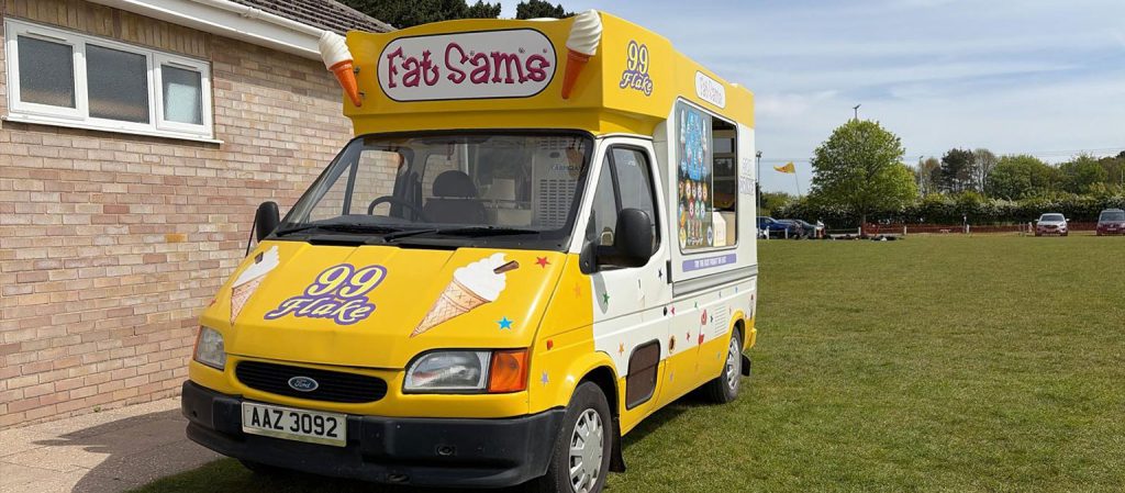 A yellow Fat Sam's Ice Cream van parked up outside a building.